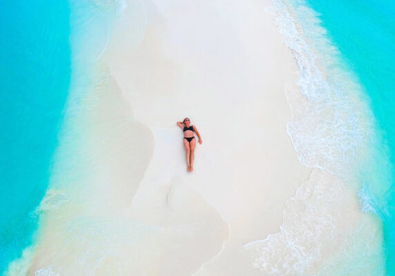 Beautiful woman tans on sandbank surrounded by turquoise ocean from above